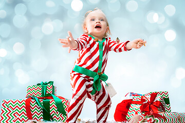 Image showing Cute baby girl 1 year old wearing santa hat posing over Christmas background. Sitting on floor with Christmas ball. Holiday season.