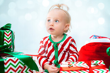 Image showing Cute baby girl 1 year old near santa hat posing over Christmas background. Sitting on floor with Christmas ball. Holiday season.