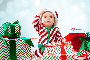 Image showing Cute baby girl 1 year old wearing santa hat posing over Christmas background. Sitting on floor with Christmas ball. Holiday season.