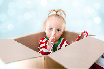 Image showing Cute baby girl 1 year old sitting at box over Christmas background. Holiday season.