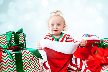 Image showing Cute baby girl 1 year old wearing santa hat posing over Christmas background. Sitting on floor with Christmas ball. Holiday season.