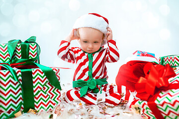 Image showing Cute baby girl 1 year old wearing santa hat posing over Christmas background. Sitting on floor with Christmas ball. Holiday season.