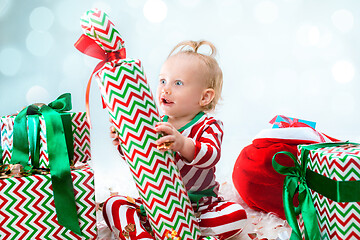 Image showing Cute baby girl 1 year old near santa hat posing over Christmas background. Sitting on floor with Christmas ball. Holiday season.