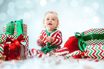 Image showing Cute baby girl 1 year old near santa hat posing over Christmas background. Sitting on floor with Christmas ball. Holiday season.