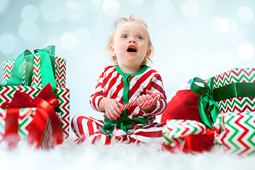 Image showing Cute baby girl 1 year old near santa hat posing over Christmas background. Sitting on floor with Christmas ball. Holiday season.