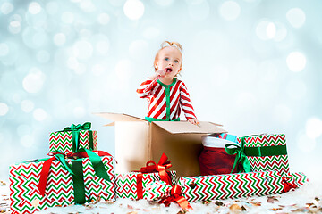 Image showing Cute baby girl 1 year old sitting at box over Christmas background. Holiday season.