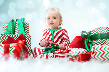 Image showing Cute baby girl 1 year old near santa hat posing over Christmas background. Sitting on floor with Christmas ball. Holiday season.
