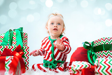 Image showing Cute baby girl 1 year old near santa hat posing over Christmas background. Sitting on floor with Christmas ball. Holiday season.