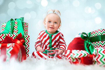 Image showing Cute baby girl 1 year old near santa hat posing over Christmas background. Sitting on floor with Christmas ball. Holiday season.