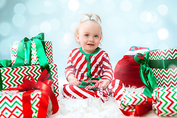 Image showing Cute baby girl 1 year old near santa hat posing over Christmas background. Sitting on floor with Christmas ball. Holiday season.