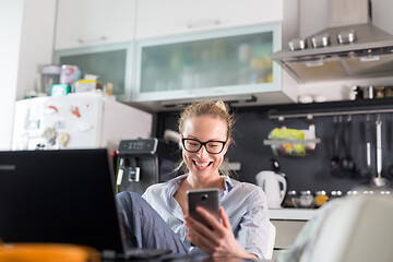 Image showing Stay at home and social distancing. Woman in her casual home clothing working remotly from her kitchen dining table in the morning. Video chatting with friend, family or business clients or partners