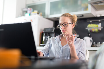 Image showing Stay at home and social distancing. Woman in her casual home clothing working remotly from kitchen dining table. Video chatting using social media with friend, family, business clients or partners