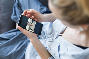 Image showing Woman at home relaxing on sofa couch using social media on phone for video chatting with her loved ones during corona virus pandemic. Stay at home, social distancing lifestyle.