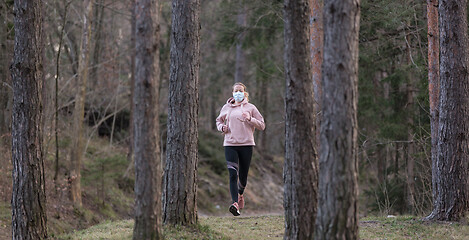 Image showing Corona virus, or Covid-19, is spreading all over the world. Portrait of caucasian sporty woman wearing a medical protection face mask while running in nature.