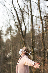 Image showing Portrait of caucasian sporty woman wearing medical protection face mask while relaxing by taking a deep breath in forest. Corona virus, or Covid-19, is spreading all over the world