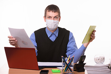 Image showing A man in a medical mask holds a paper document in one hand, and a tablet computer in the other