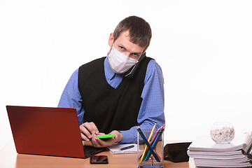 Image showing An office worker in a protective medical mask is talking on the phone, counting on a calculator and looking at the frame