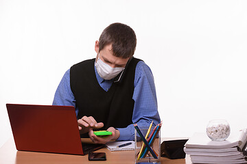 Image showing An office employee in a protective medical mask is talking on the phone, counting on a calculator