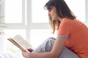 Image showing Girl at home by the window in the bedroom reads her favorite book