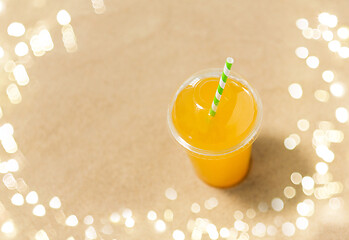 Image showing cup of orange juice with straw on beach sand