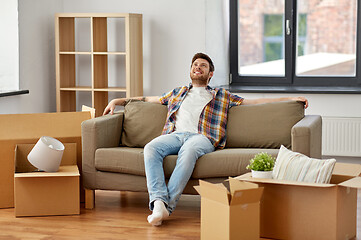 Image showing happy man with boxes sitting on sofa at new home