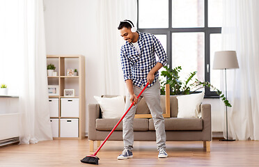 Image showing man in headphones with broom cleaning at home