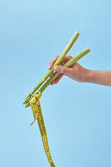 Image showing Female\'s hand with asparagus sticks is taking measure tape.