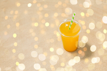 Image showing cup of orange juice with straw on beach sand