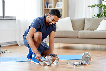 Image showing smiling indian man assembling dumbbells at home