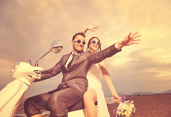 Image showing just married couple on the beach ride white scooter