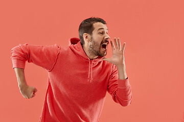 Image showing Isolated on coral young casual man shouting at studio