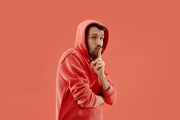 Image showing The young man whispering a secret behind her hand over coral background