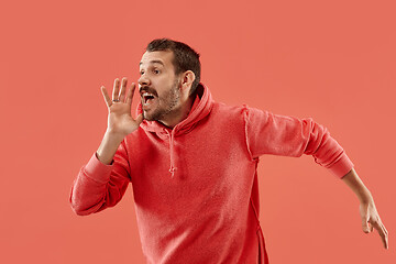 Image showing Isolated on coral young casual man shouting at studio