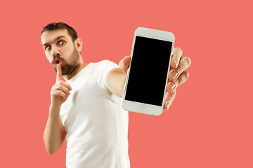 Image showing Young handsome man showing smartphone screen isolated on coral background in shock with a surprise face