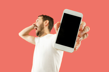 Image showing Young handsome man showing smartphone screen isolated on coral background in shock with a surprise face