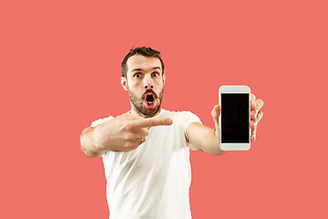 Image showing Young handsome man showing smartphone screen isolated on coral background in shock with a surprise face