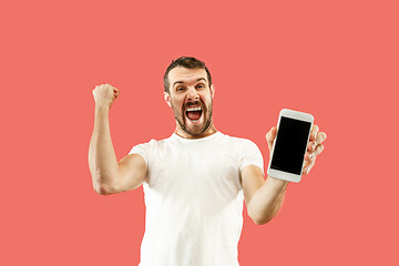 Image showing Young handsome man showing smartphone screen isolated on coral background in shock with a surprise face