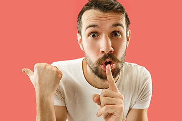 Image showing The young man whispering a secret behind her hand over coral background