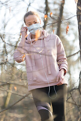 Image showing Portrait of caucasian sporty woman wearing medical protection face mask while walking in park, relaxing and listening to music. Corona virus, or Covid-19, is spreading all over the world