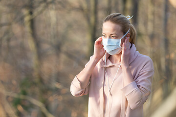 Image showing Portrait of caucasian sporty woman wearing medical protection face mask while walking in park, relaxing and listening to music. Corona virus, or Covid-19, is spreading all over the world