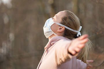 Image showing Portrait of caucasian sporty woman wearing medical protection face mask while relaxing by taking a deep breath in forest. Corona virus, or Covid-19, is spreading all over the world