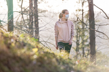 Image showing Corona virus, or Covid-19, is spreading all over the world. Portrait of caucasian sporty woman wearing a medical protection face mask while walking in the forest. Corona virus.