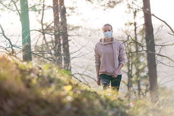 Image showing Corona virus, or Covid-19, is spreading all over the world. Portrait of caucasian sporty woman wearing a medical protection face mask while walking in the forest. Corona virus.