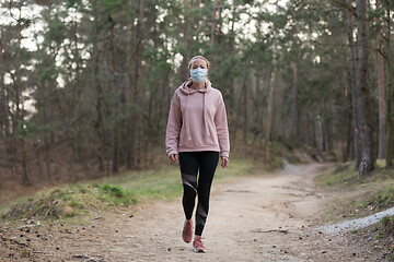 Image showing Corona virus, or Covid-19, is spreading all over the world. Portrait of caucasian sporty woman wearing a medical protection face mask while walking in the forest. Corona virus.