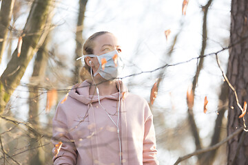 Image showing Portrait of caucasian sporty woman wearing medical protection face mask while walking in park, relaxing and listening to music. Corona virus, or Covid-19, is spreading all over the world