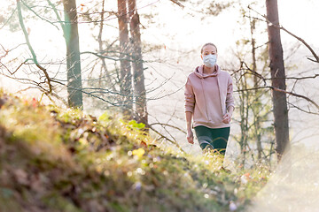 Image showing Corona virus, or Covid-19, is spreading all over the world. Portrait of caucasian sporty woman wearing a medical protection face mask while walking in the forest. Corona virus.