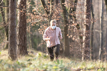 Image showing Corona virus, or Covid-19, is spreading all over the world. Portrait of caucasian sporty woman wearing a medical protection face mask while running in nature.