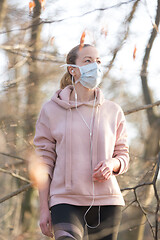 Image showing Portrait of caucasian sporty woman wearing medical protection face mask while walking in park, relaxing and listening to music. Corona virus, or Covid-19, is spreading all over the world