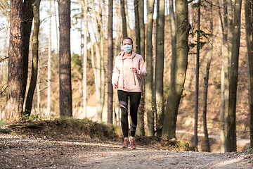 Image showing Corona virus, or Covid-19, is spreading all over the world. Portrait of caucasian sporty woman wearing a medical protection face mask while running in nature.