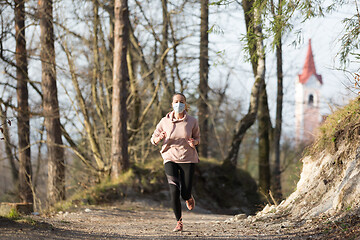 Image showing Corona virus, or Covid-19, is spreading all over the world. Portrait of caucasian sporty woman wearing a medical protection face mask while running in nature.